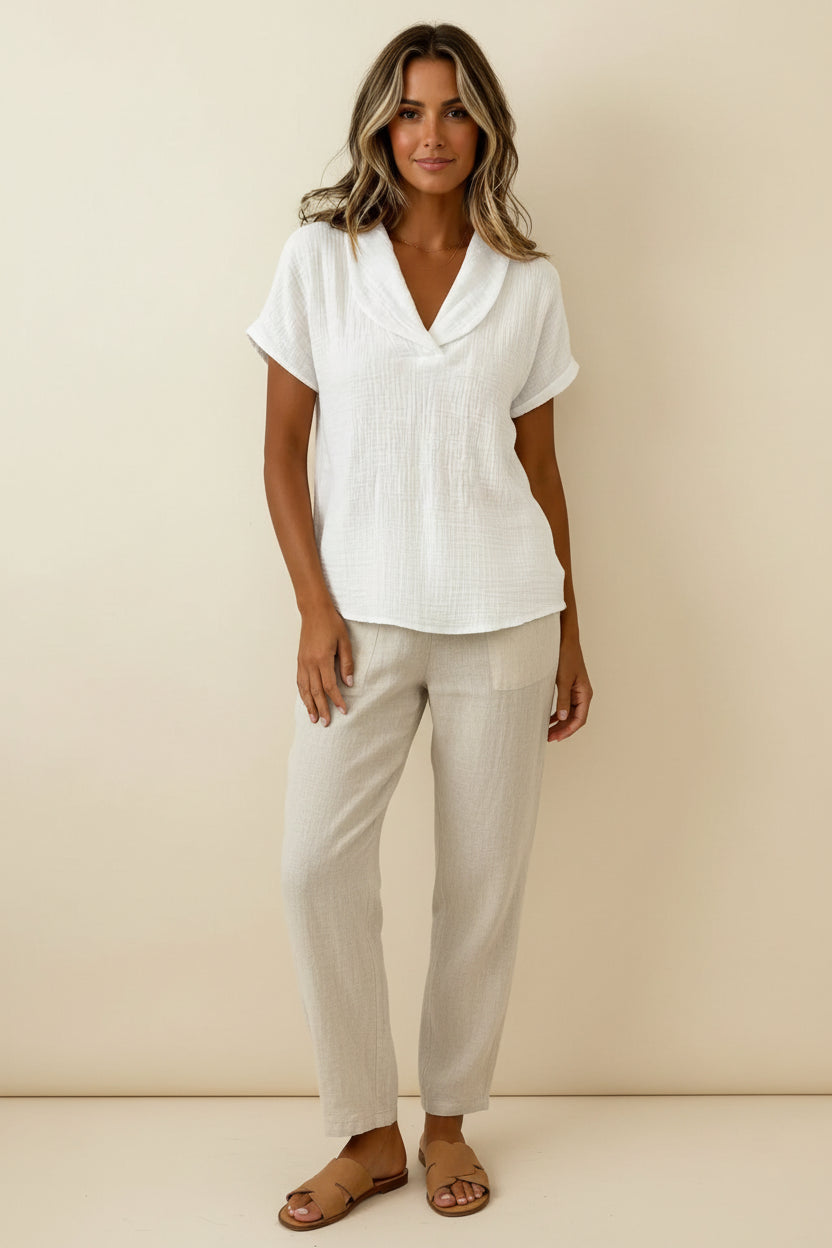 A close-up of a woman wearing a white textured short-sleeve top with a wide collar and V-neckline.