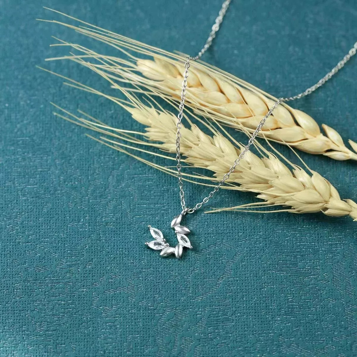 Silver necklace with a leaf pendant on a blue background with wheat
