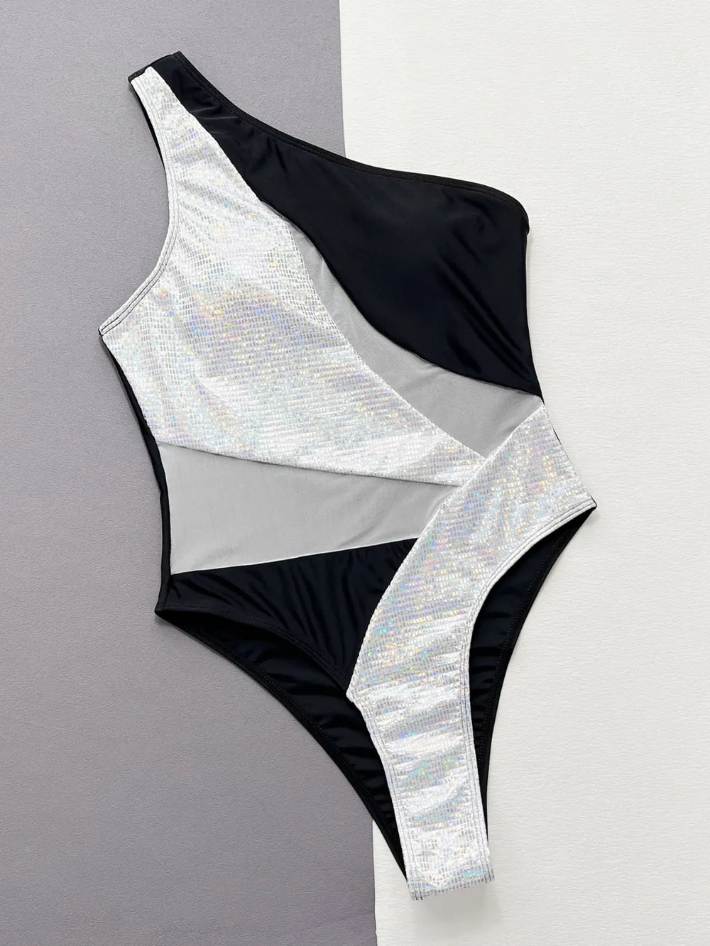 Front of the one-shoulder swimsuit laid flat, black, white and silver sequin panels, gray backdrop