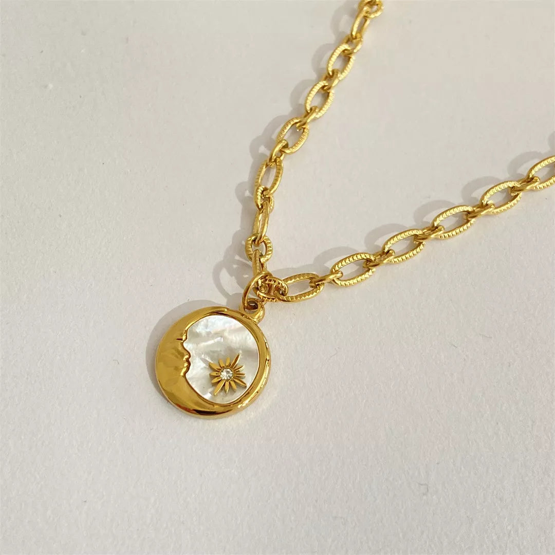 Gold necklace with a moon and sun pendant on a light gray background