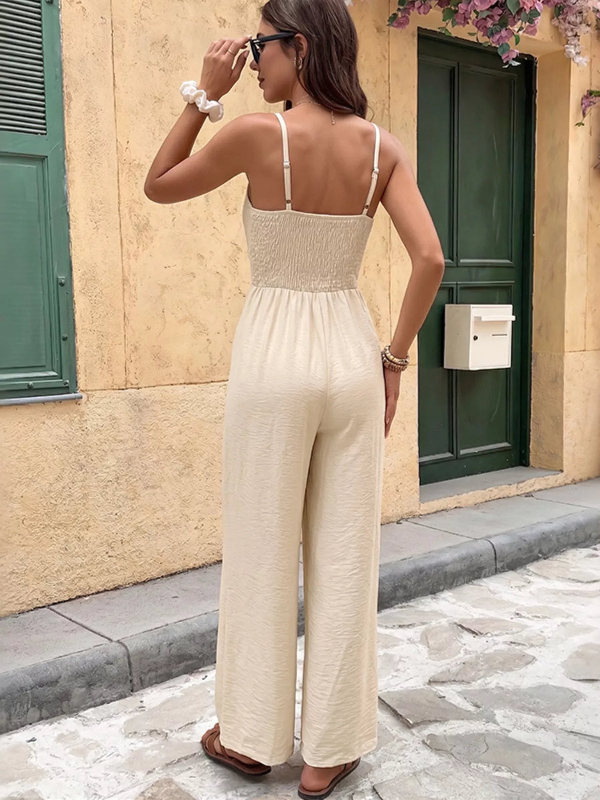 Woman in a beige jumpsuit standing on a street with a building in the background