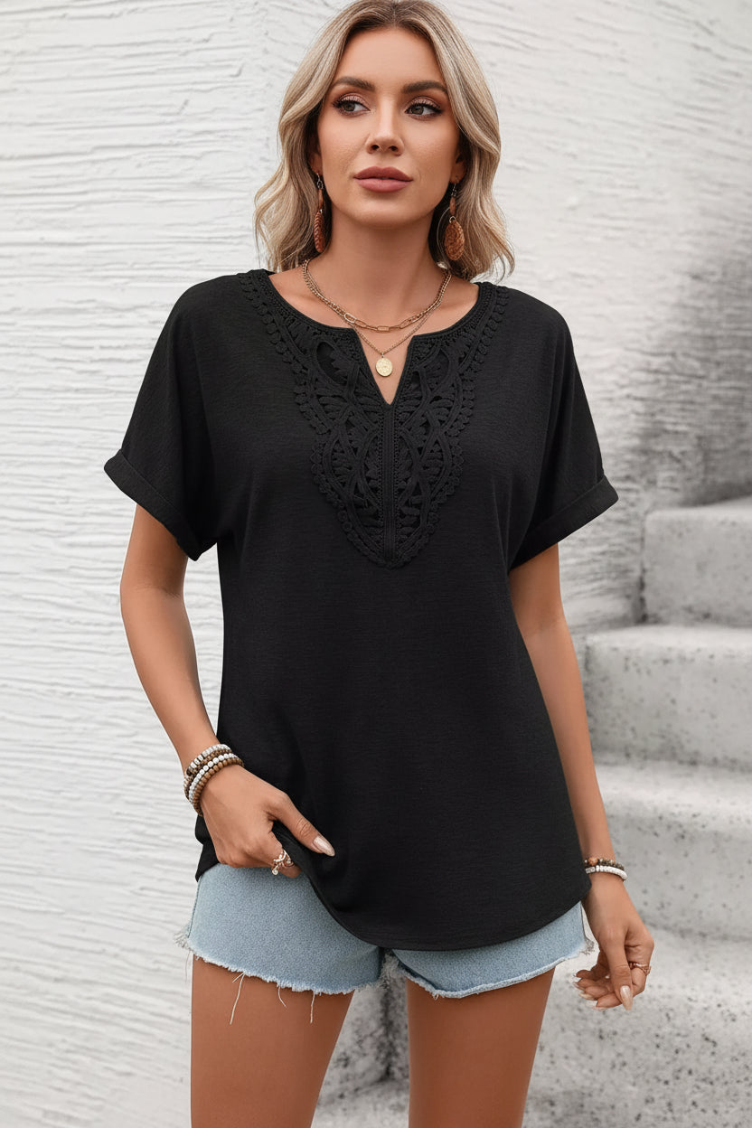 Woman wearing a black lace-trimmed top and denim shorts against a light stone wall.