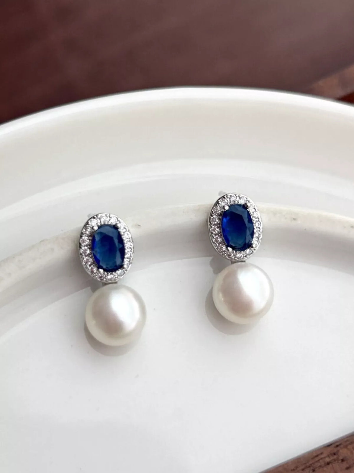 Pair of earrings with blue gemstones and pearls on a white surface