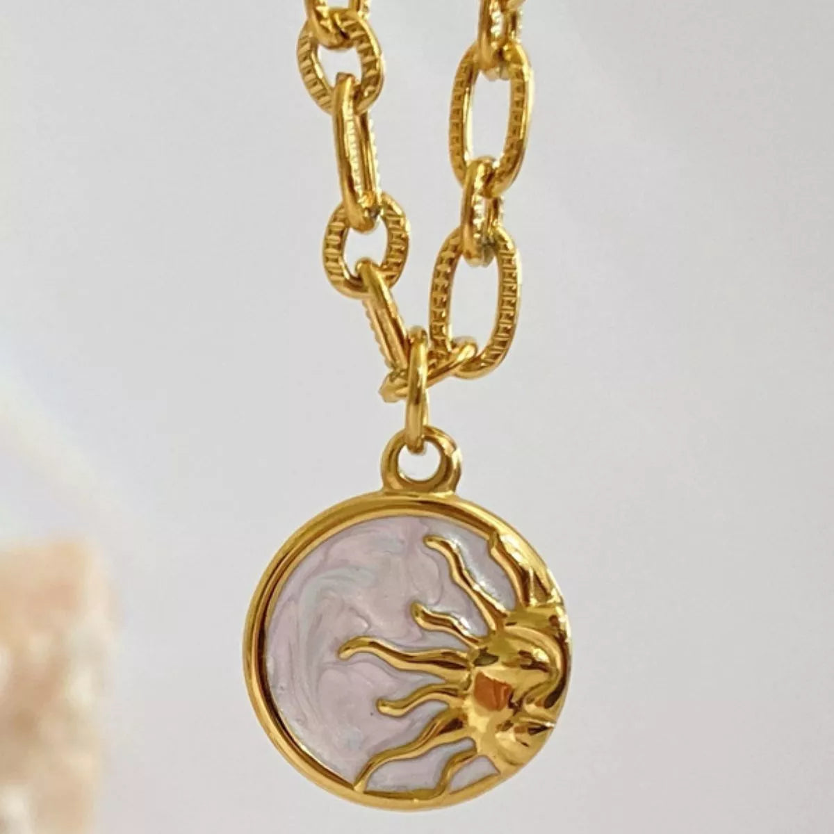 Gold necklace with a sun pendant on a light gray background