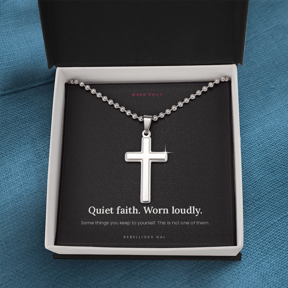 Steel cross pendant on a ball chain filling a black gift box, viewed overhead