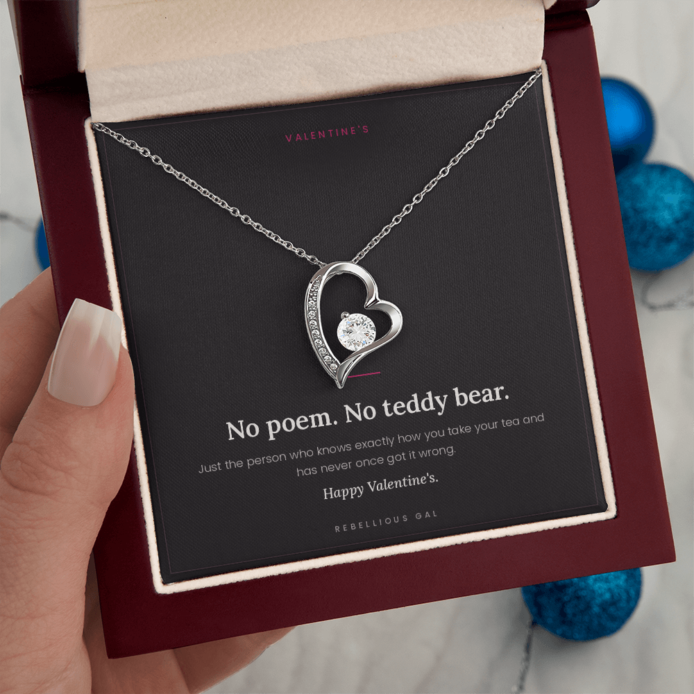 Hand holding the open box, white gold heart pendant on the card, blue ornaments behind