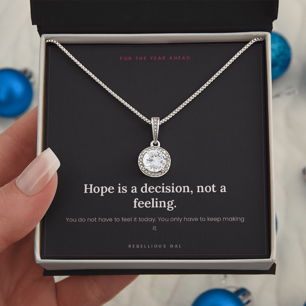 Hand holding the open gift box, silver halo pendant on card, blue ornaments behind