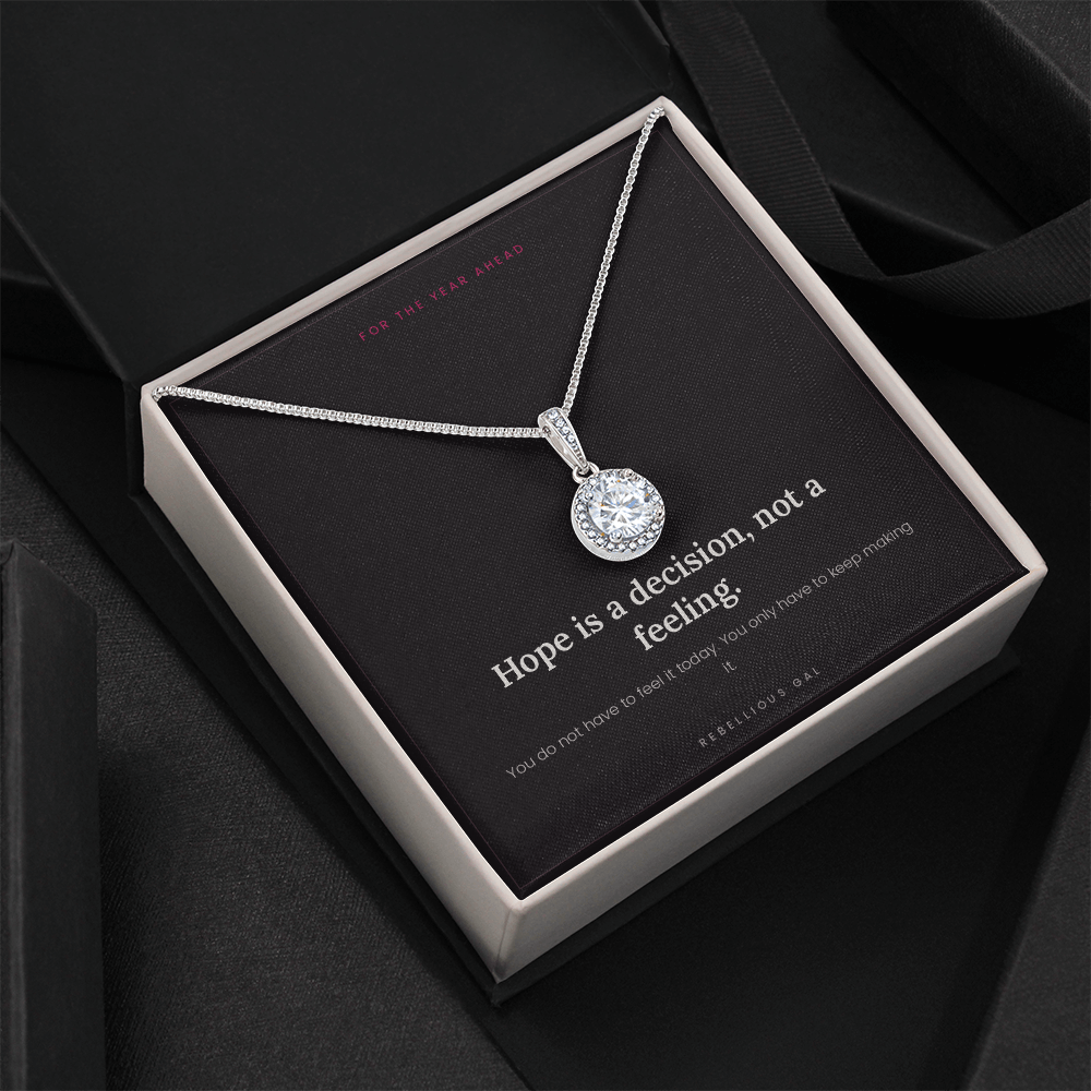 Open cream box tilted on dark fabric, silver halo pendant on the message card