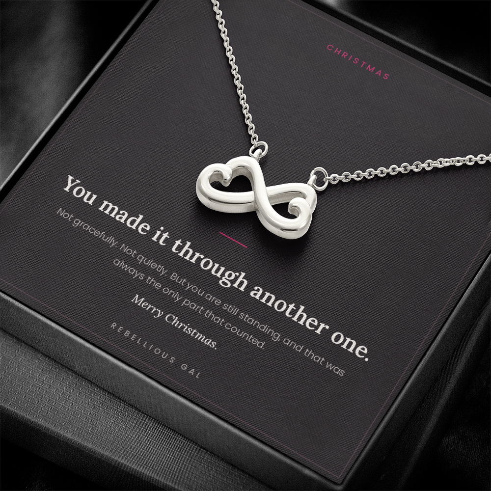 Close-up of the silver infinity heart pendant across the black message card in a dark box