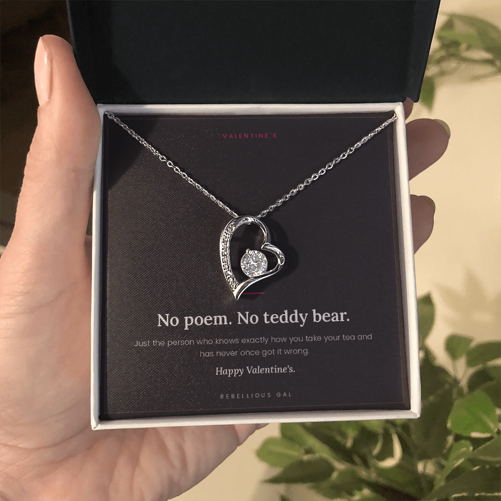 aHand holding the open gift box with the silver heart pendant and No Poem card