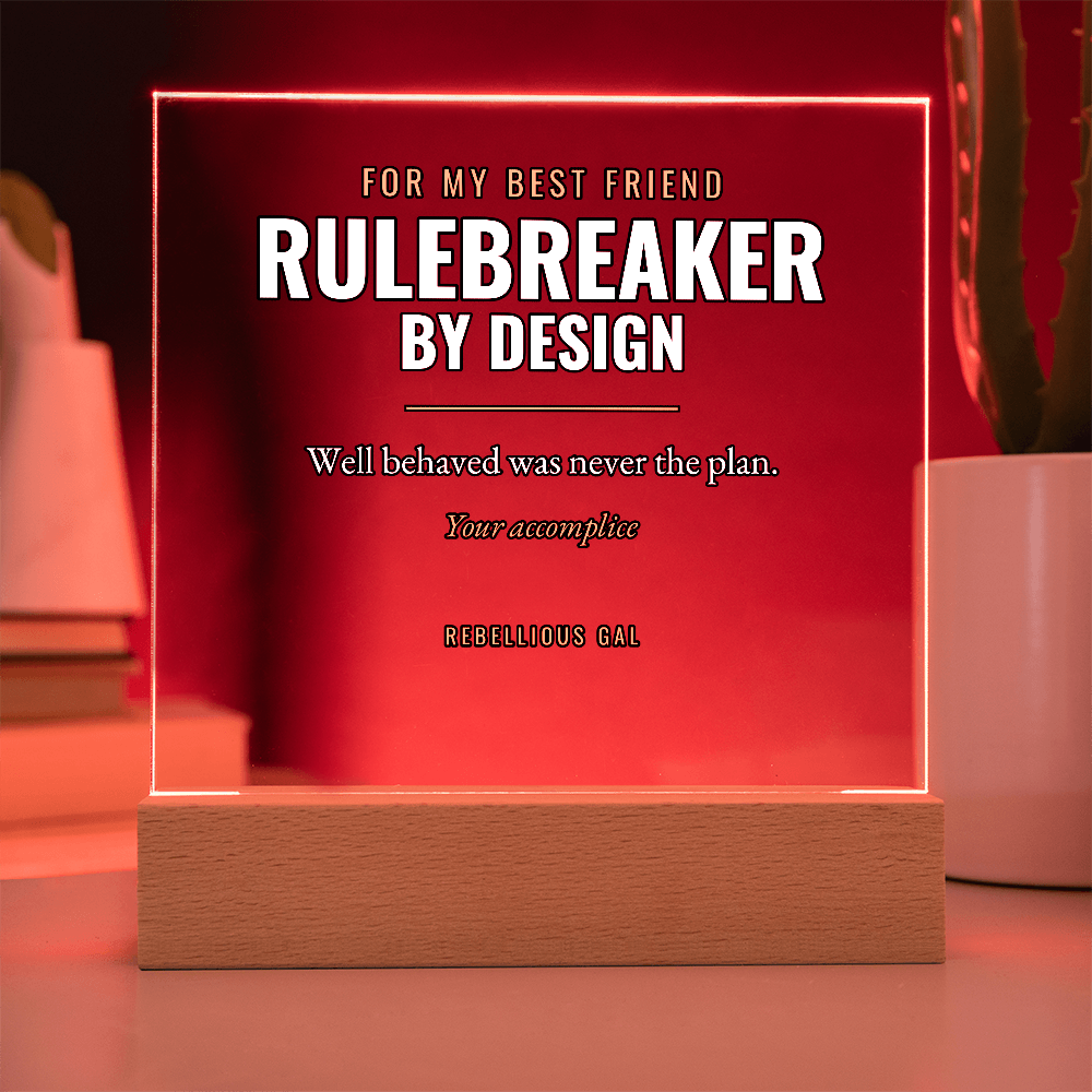 Crimson-lit Rulebreaker by Design plaque glowing above its wood base, planter behind