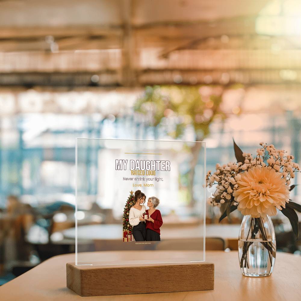 Peach blooms in a glass vase beside the clear plaque, blurred warm interior behind