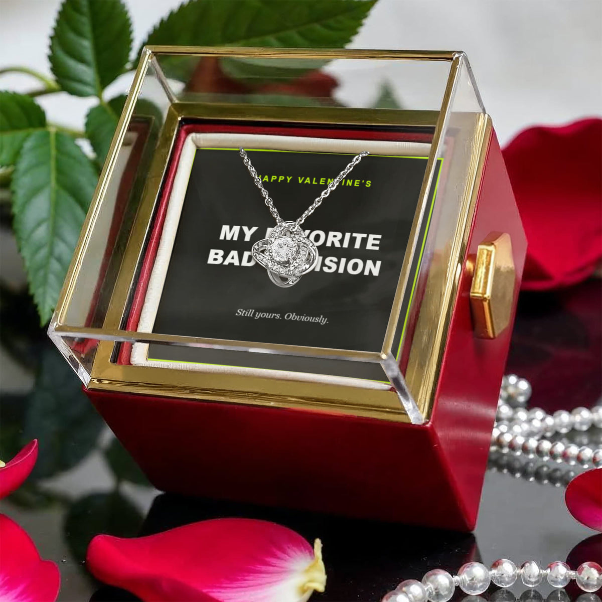 Red gift box among rose petals and pearls, silver love knot pendant on its black card