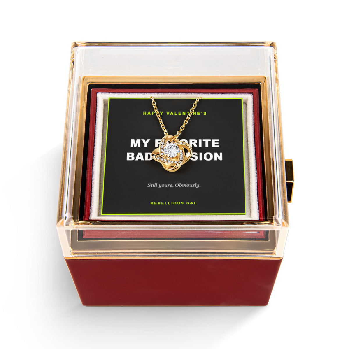 Gold love knot pendant with a clear solitaire, hanging over the card inside the red box