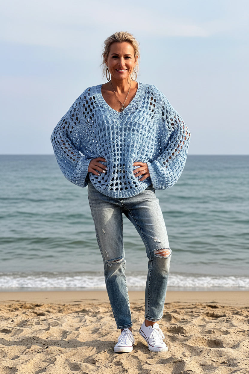 Person wearing a light blue crochet sweater by a body of water