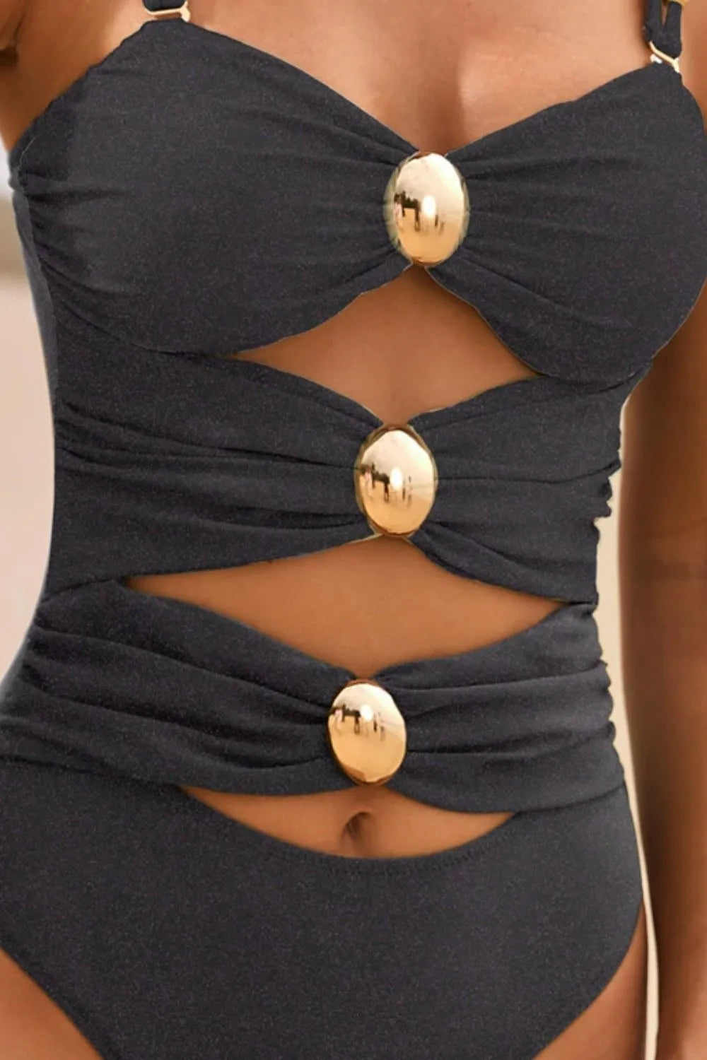 Black swimsuit with gold buttons on a neutral background