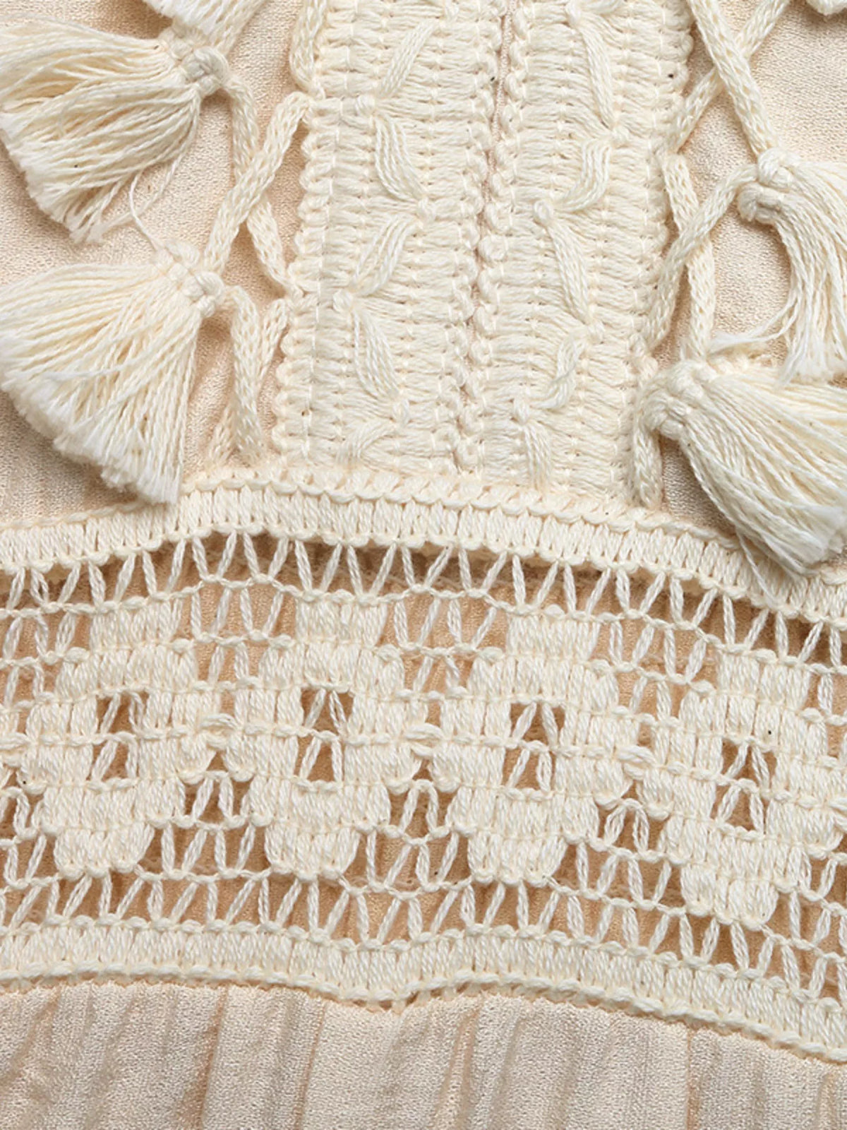 Close-up of beige fabric with intricate lace detailing and tassels.