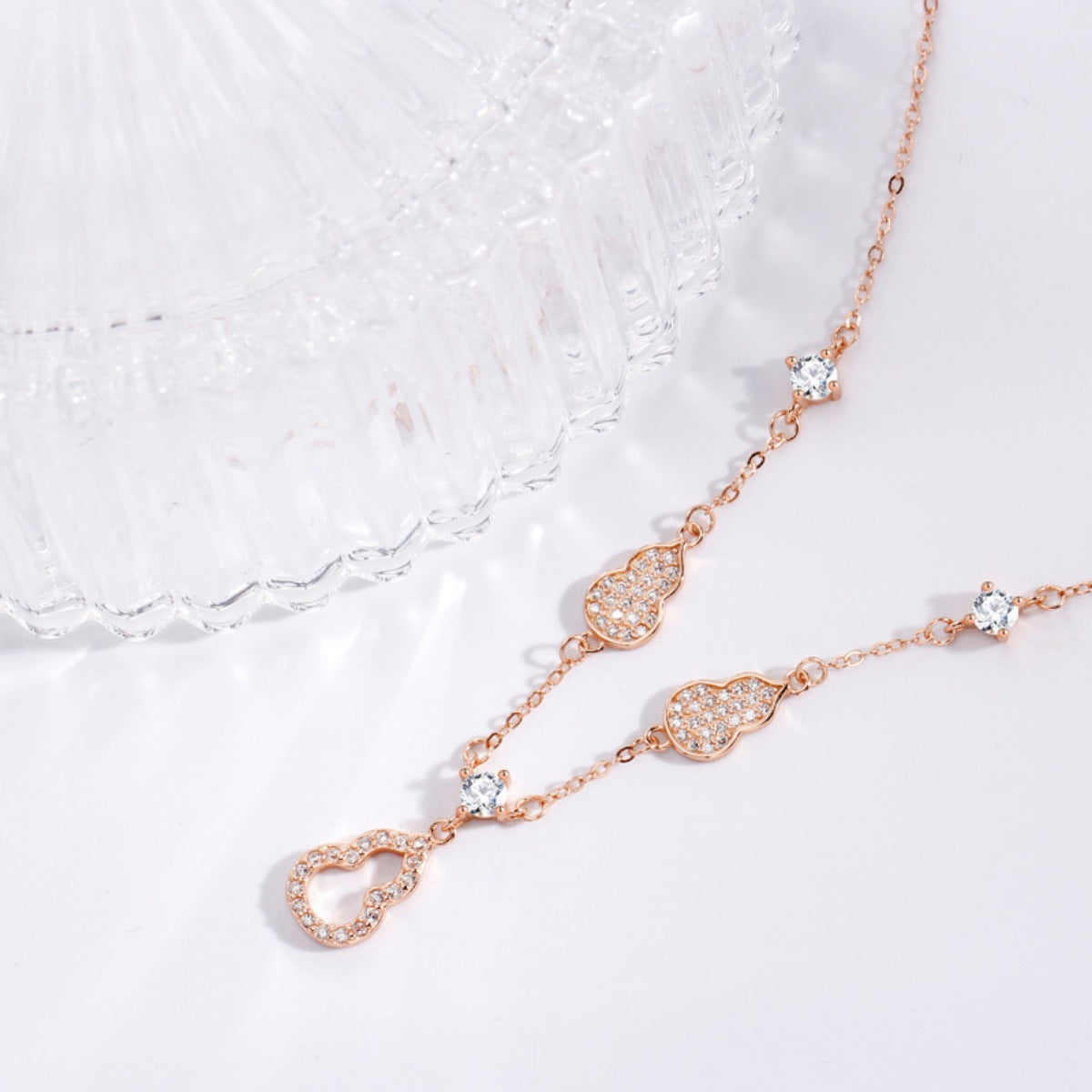 Rose gold necklace with heart and teardrop designs on a white lace background
