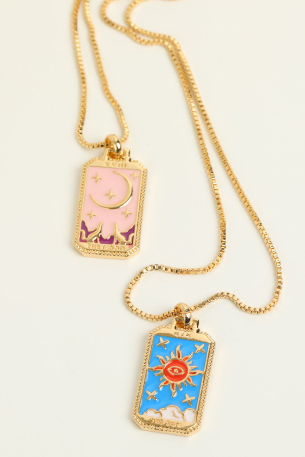 Two rectangular pendants on gold chains against a white background