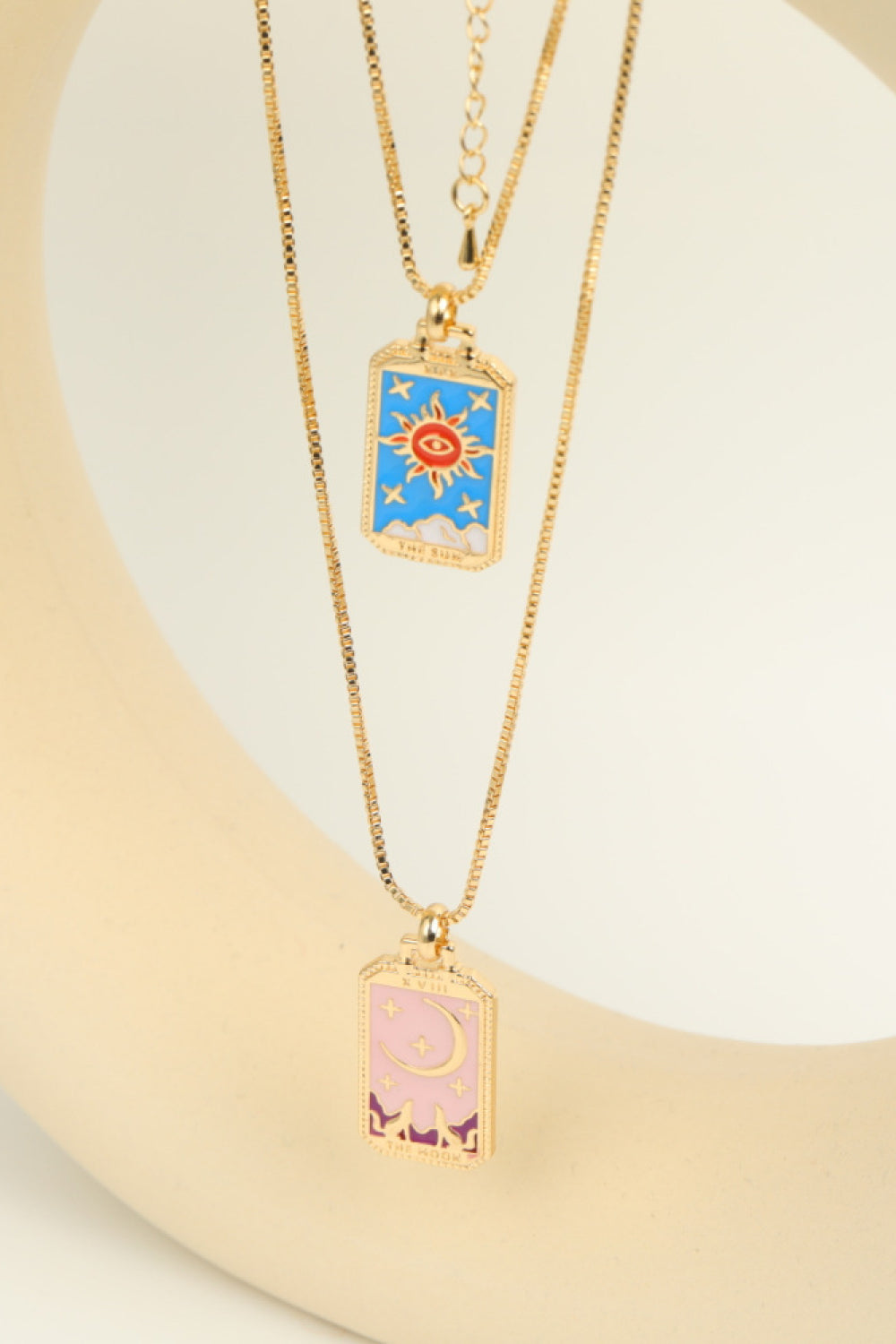 Two gold necklaces with colorful pendant designs on a white background
