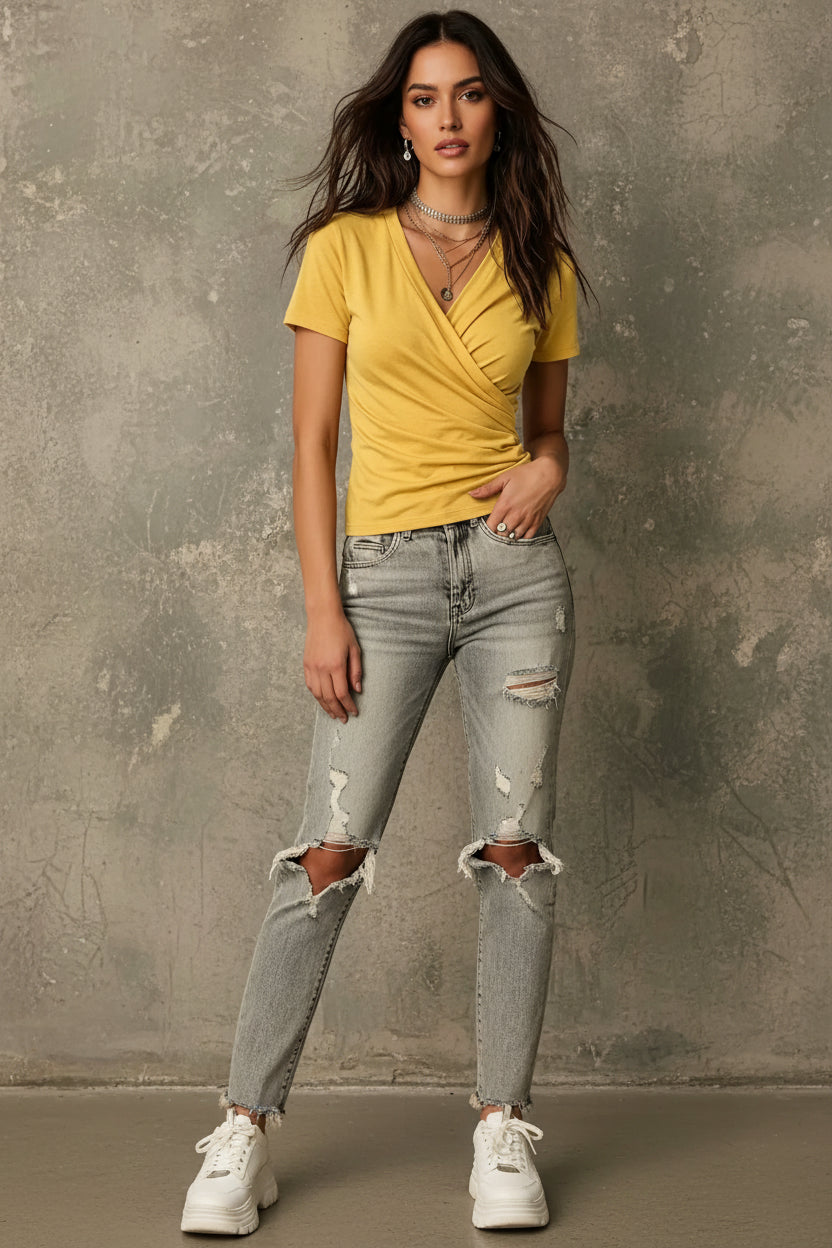 Woman wearing a yellow top and gray jeans against a textured wall.