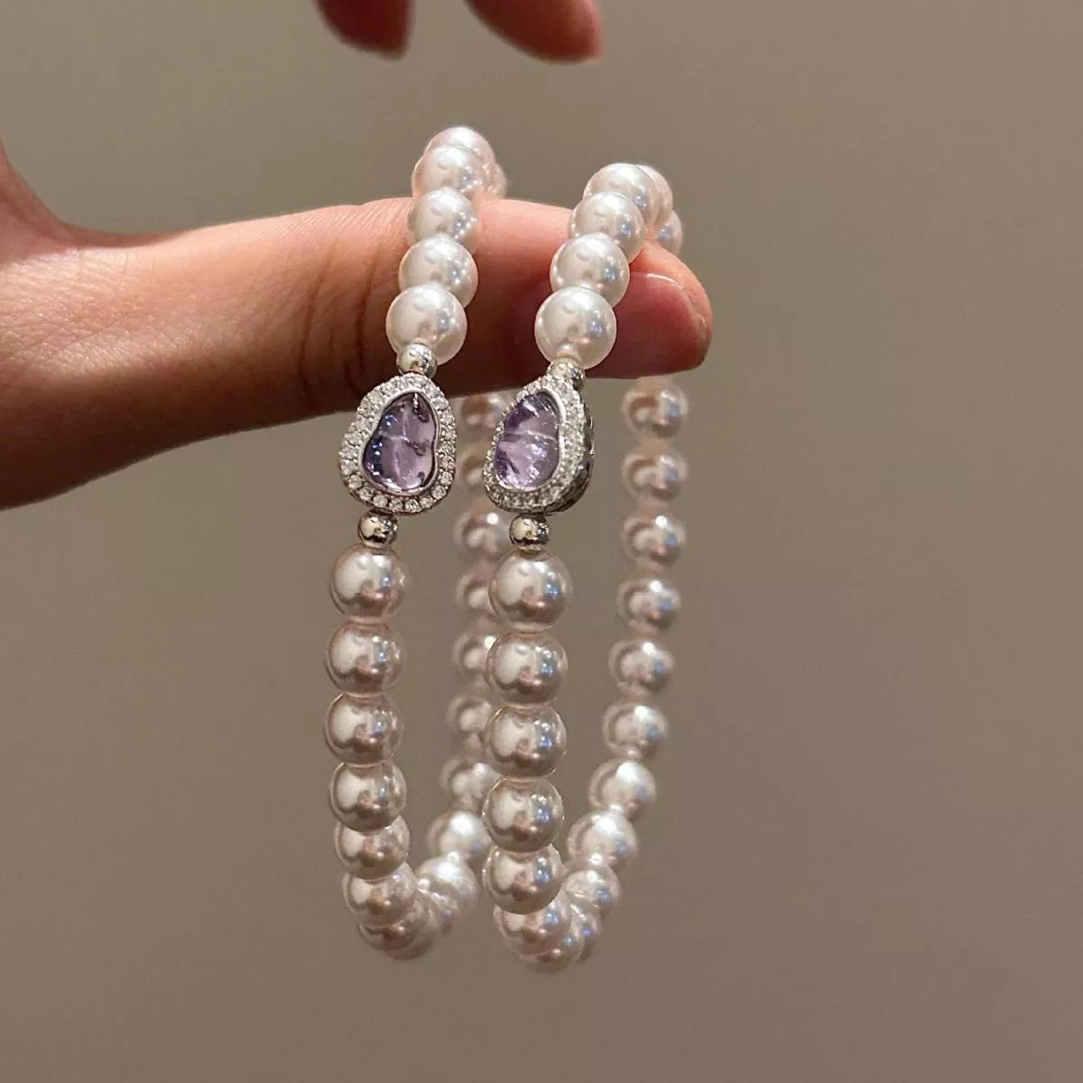 Pearl bracelets with purple gemstones held by a hand against a neutral background