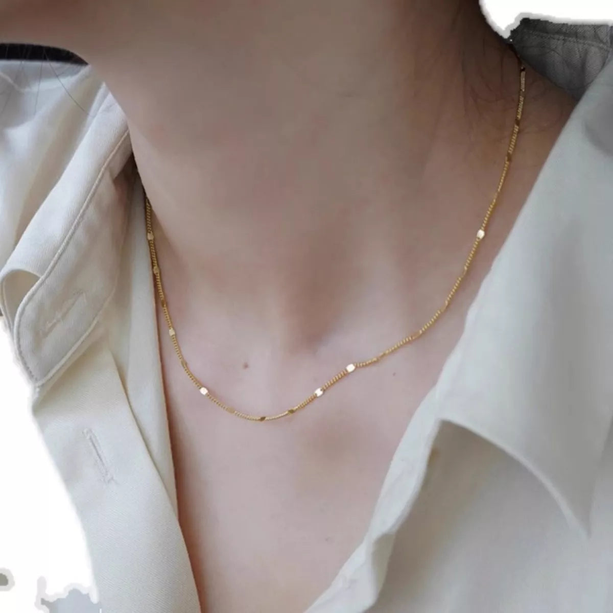 Gold necklace worn by a person with a light background