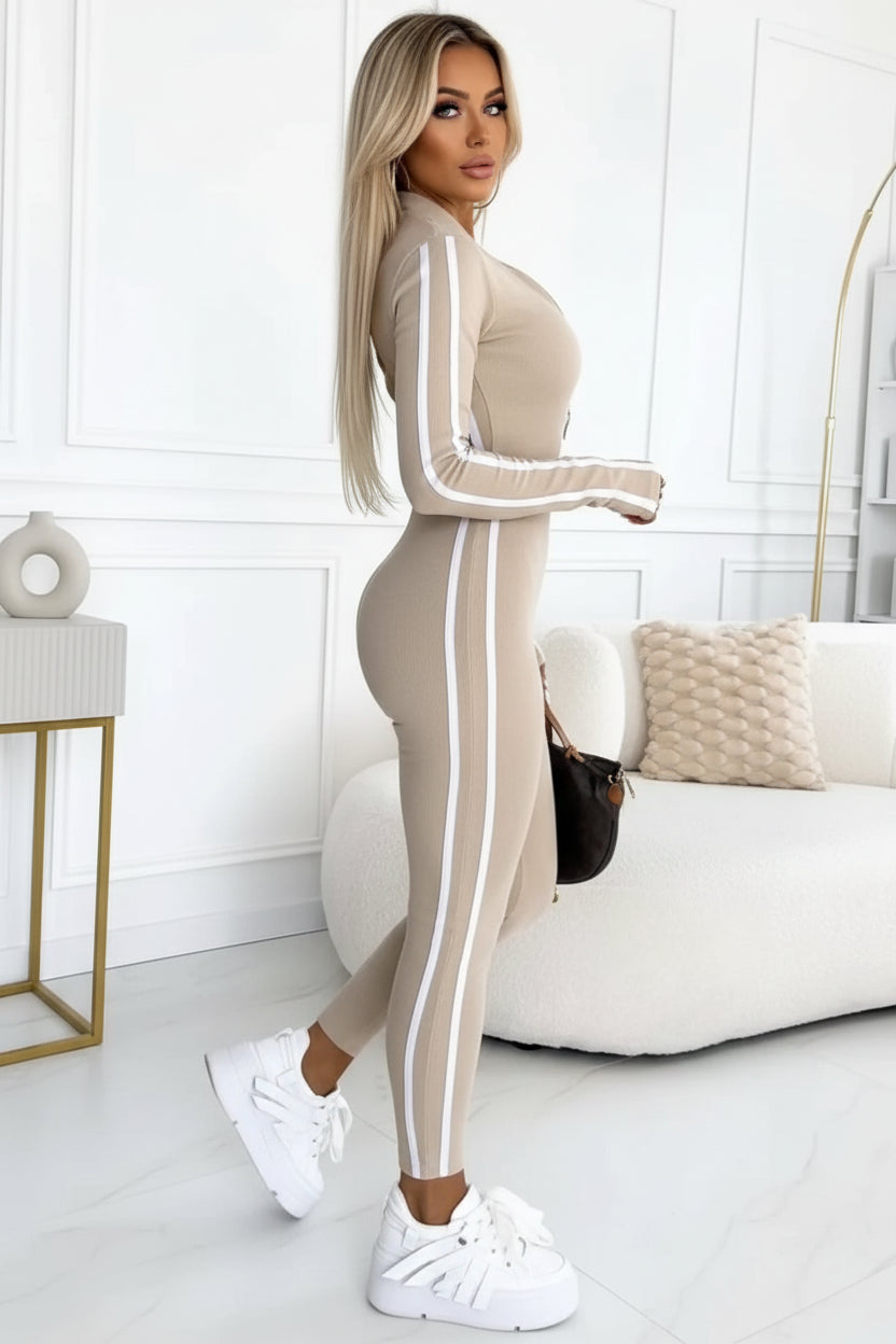 Person wearing a beige tracksuit with white stripes, sitting on a white couch in a minimalistic room.