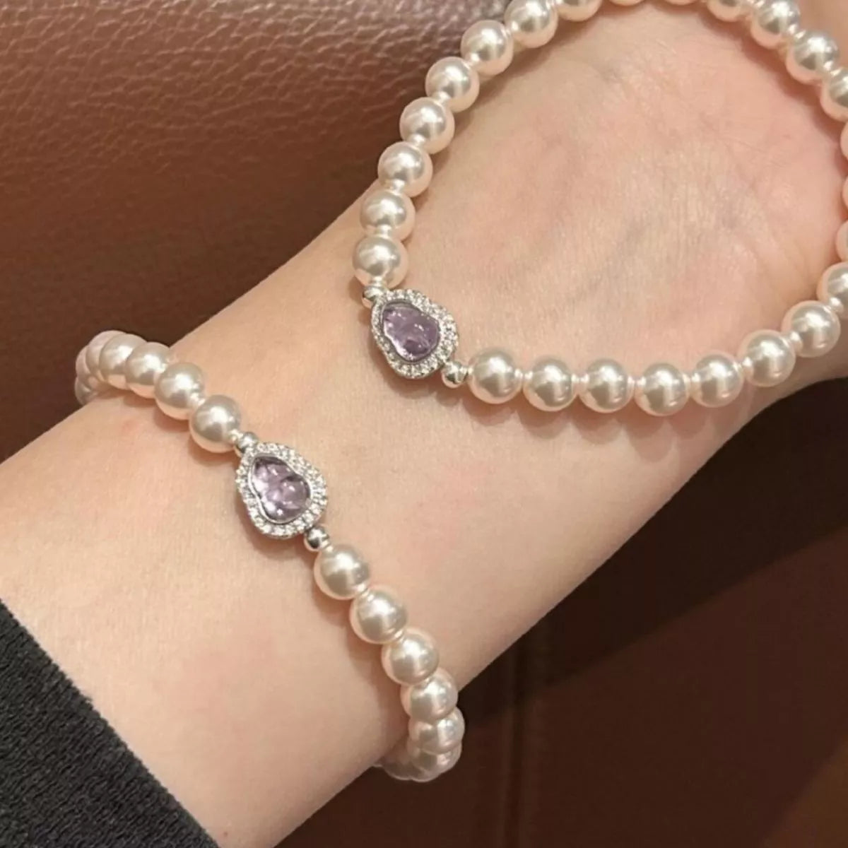 Pearl bracelet with purple gemstones on a wrist against a brown background