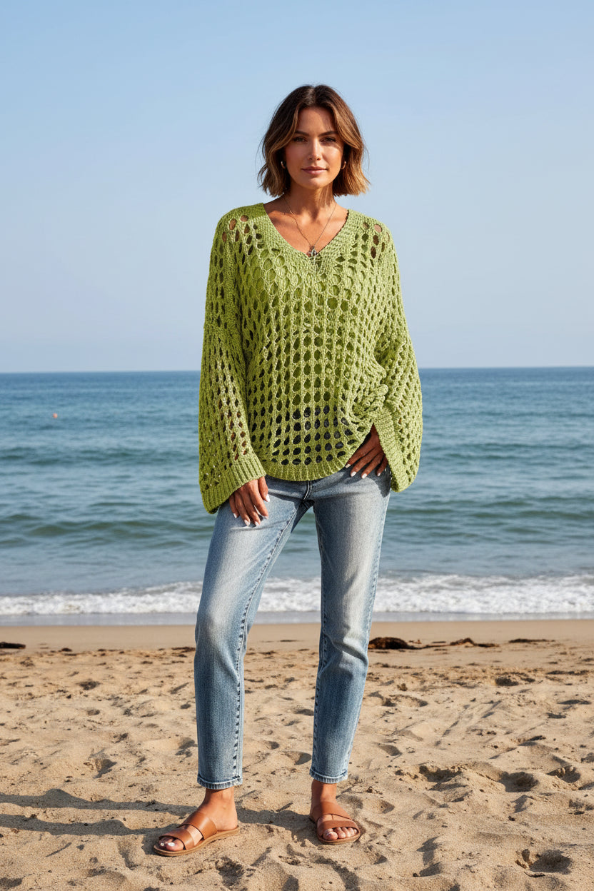 Person wearing a green knitted sweater with a textured pattern, standing against a blurred natural background.