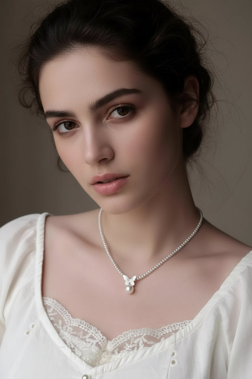 Pearl necklace with a butterfly pendant worn by a person in a white lace top.
