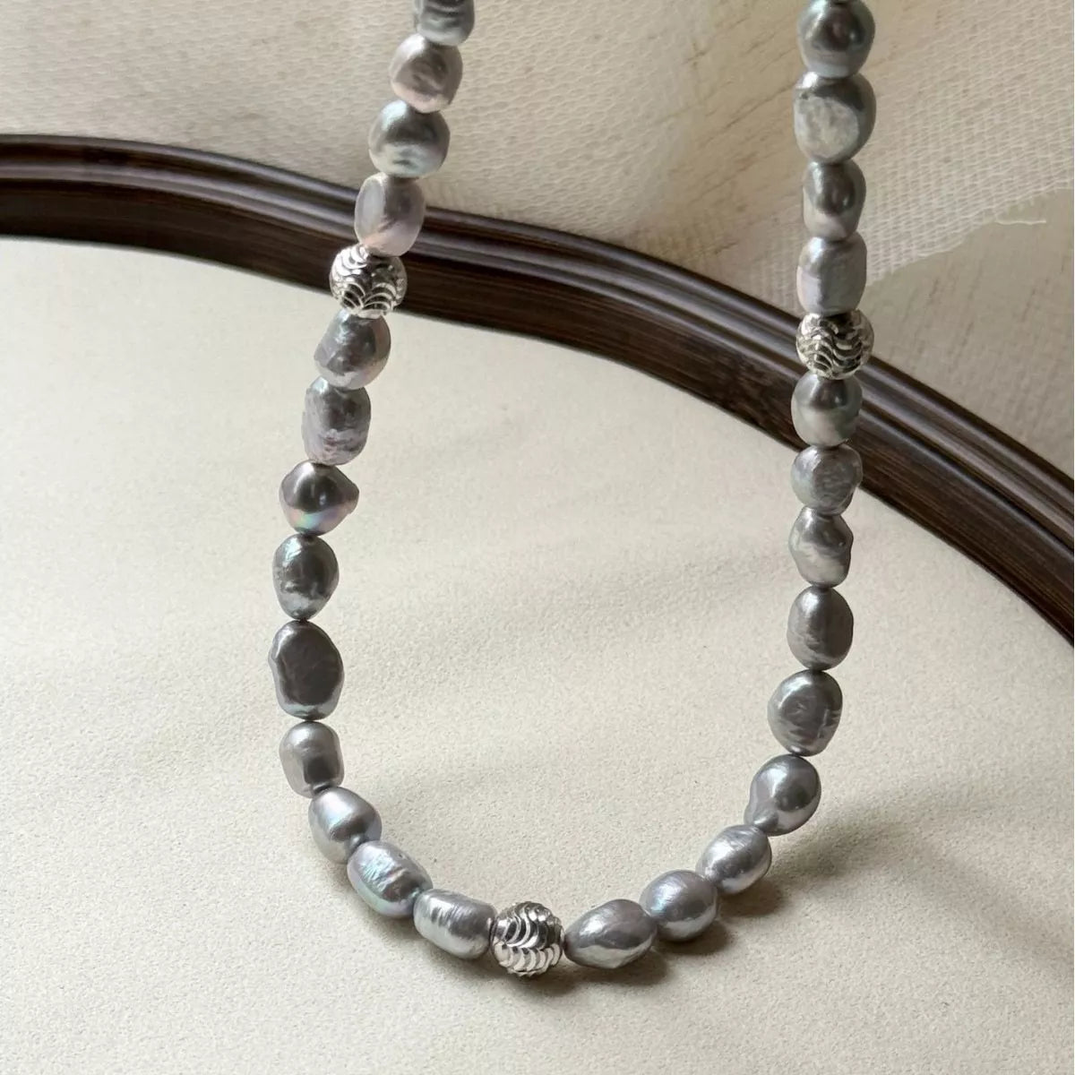 Silver beaded necklace on a beige surface with a neutral background