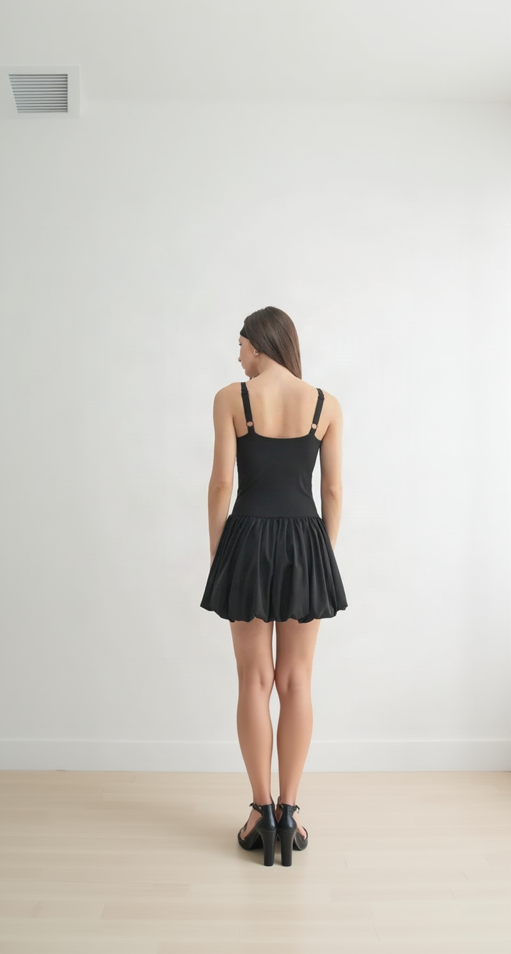 Model seen from behind in a black bubble-hem mini dress, strappy heels, pale wood floor