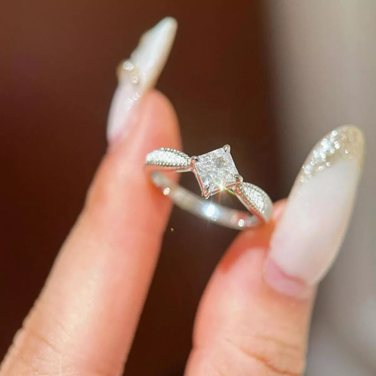 Silver ring with a diamond held between fingers against a blurred background