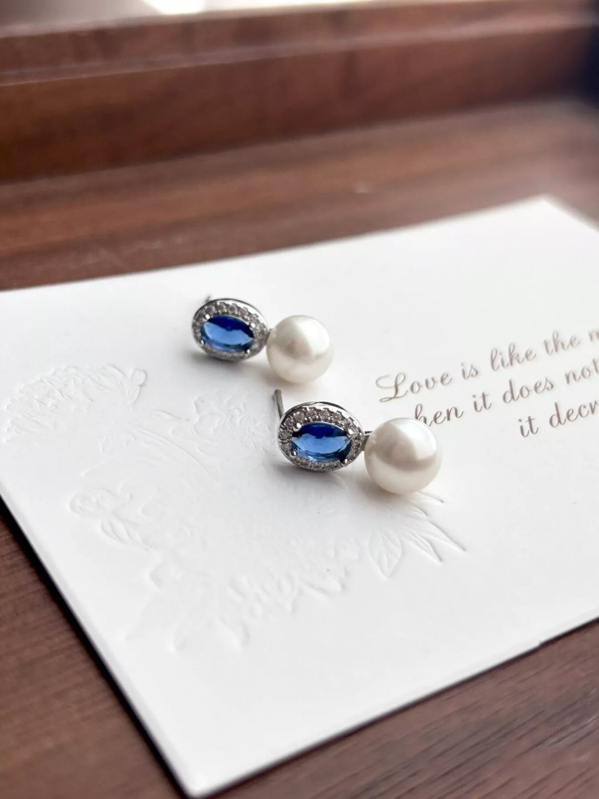Pearl and blue gemstone earrings on a white card with text
