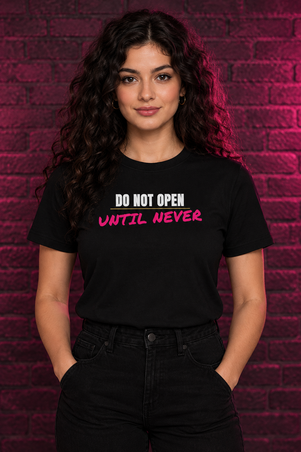 Woman with long dark curls in the black Do Not Open Until Never tee, brick wall