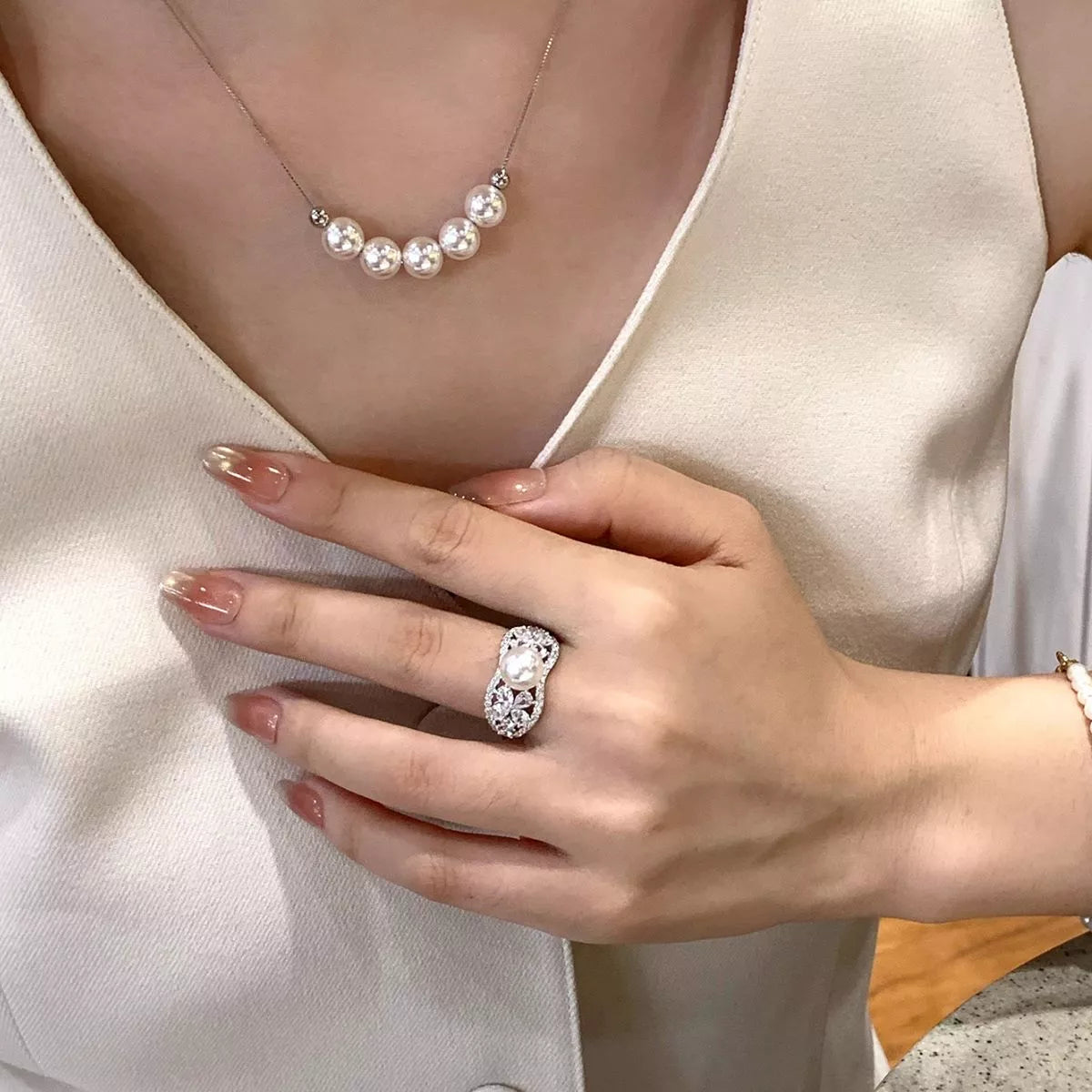 Close-up of a hand wearing a diamond ring with a pearl necklace.