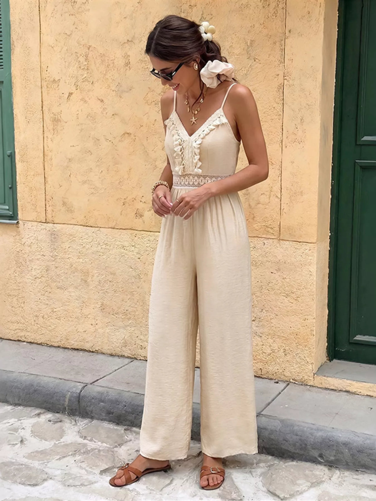 Woman wearing a beige jumpsuit standing against a beige wall.