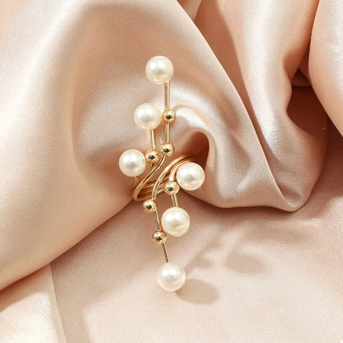 Gold earring with pearls on a soft pink fabric background