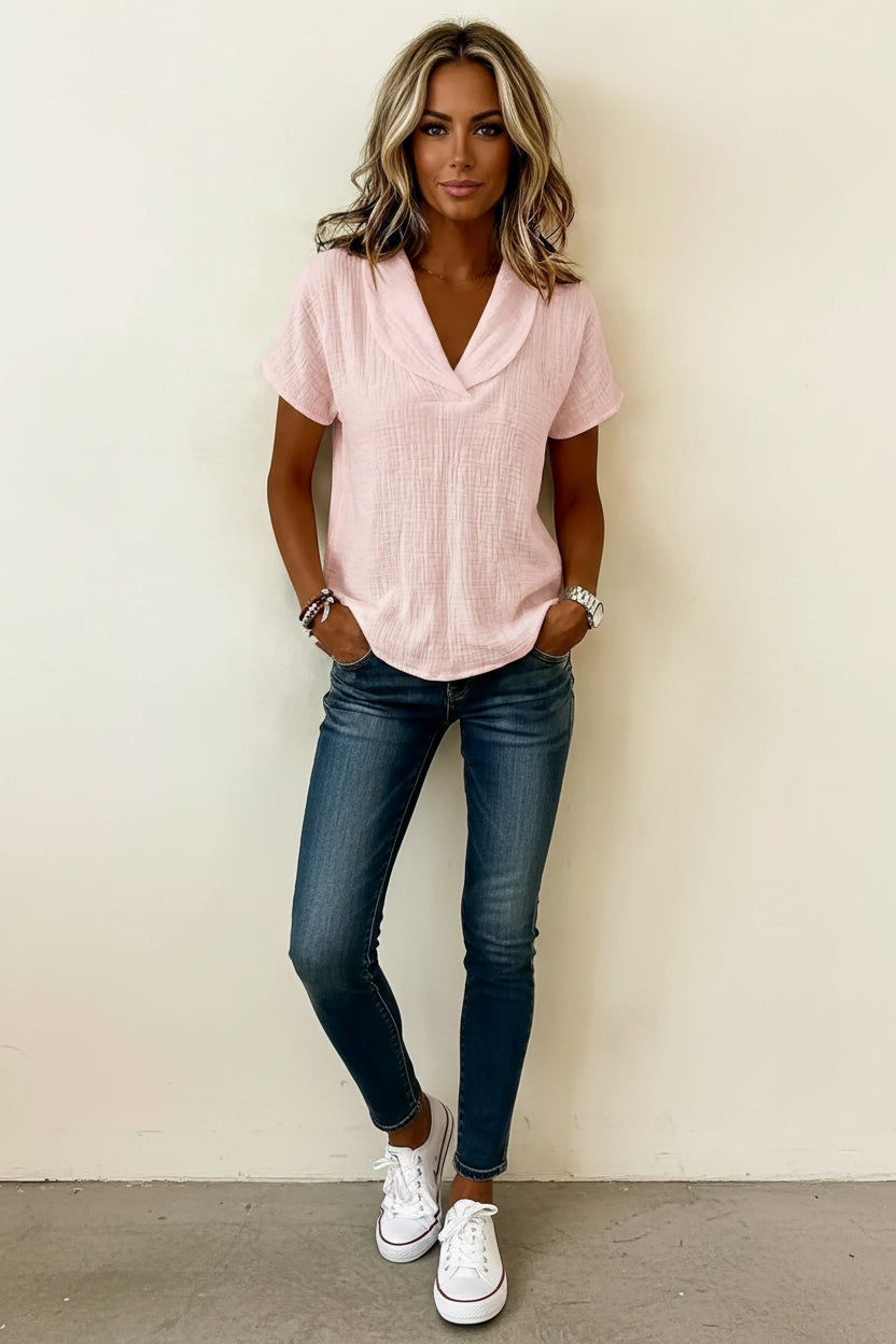 Person wearing a light pink short-sleeve top with a neutral background
