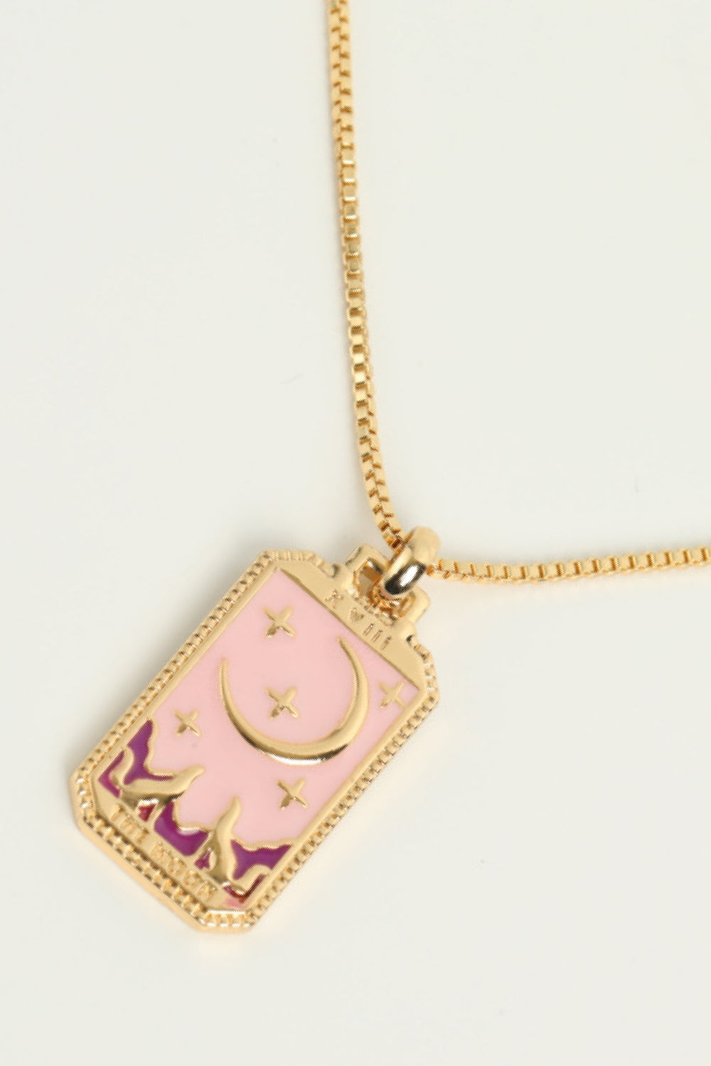 Necklace with a pink and gold pendant on a light beige background