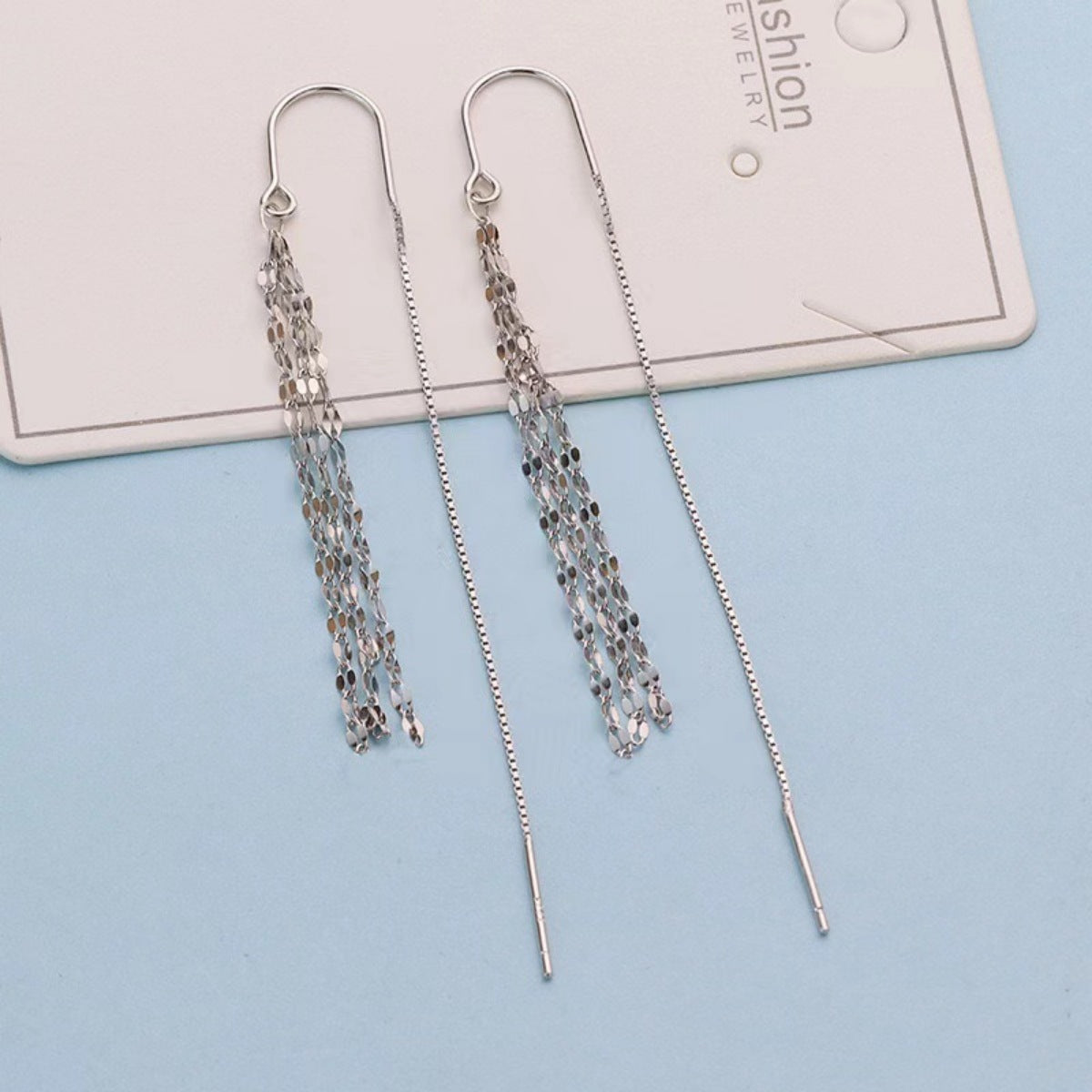 Silver chain earrings on a light blue background with a card in the background