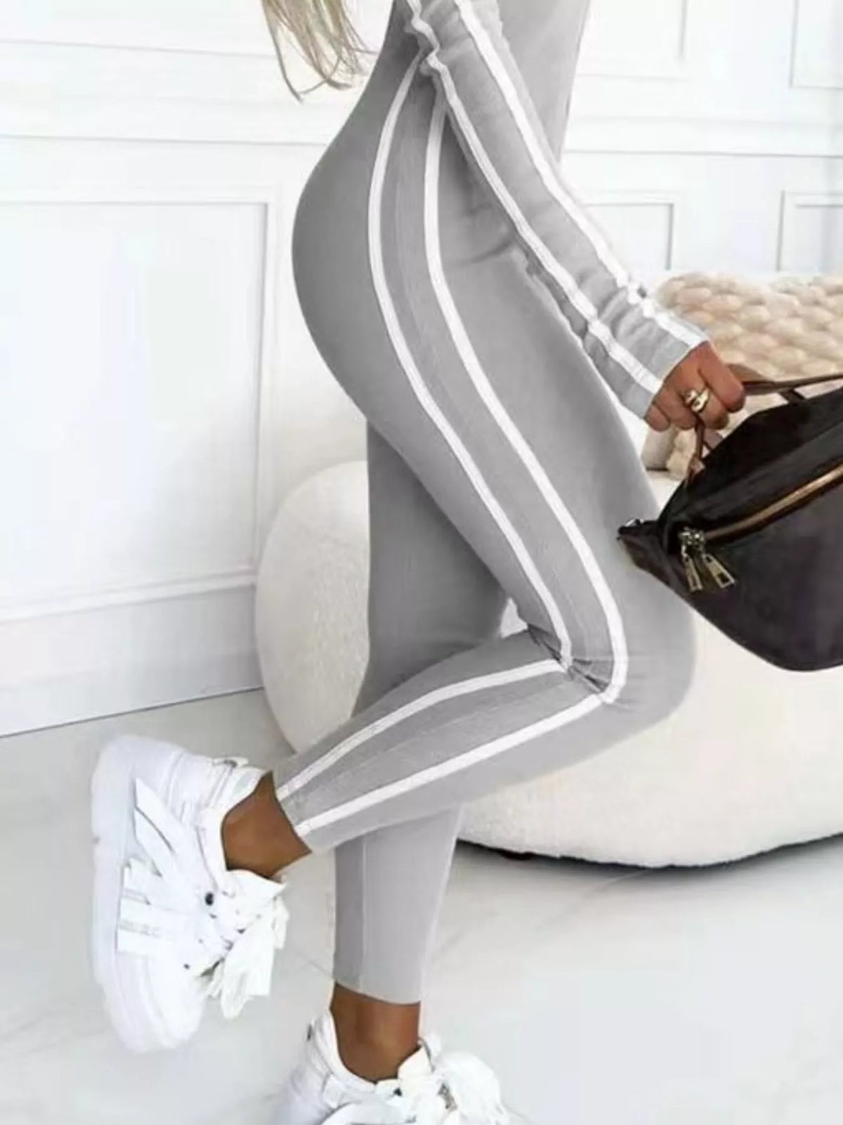 Person wearing gray jogger pants with white stripes and white sneakers, sitting on a white couch.