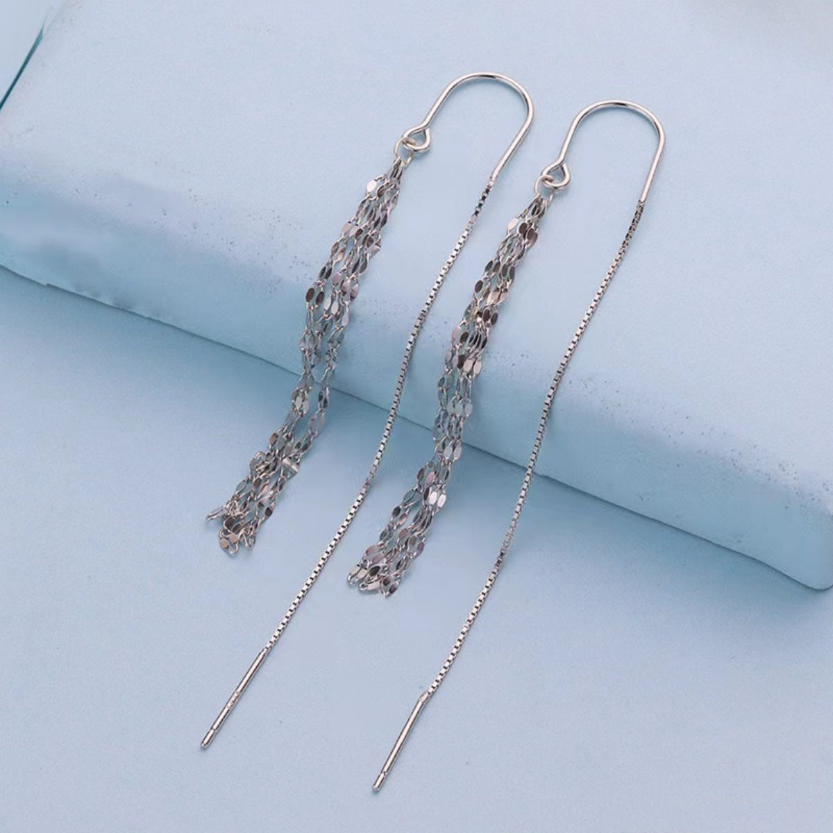 Silver chain earrings on a light blue surface