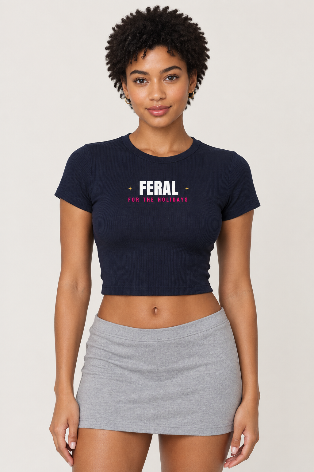 Woman with short dark coils in the navy Feral for the Holidays crop tee, pale backdrop