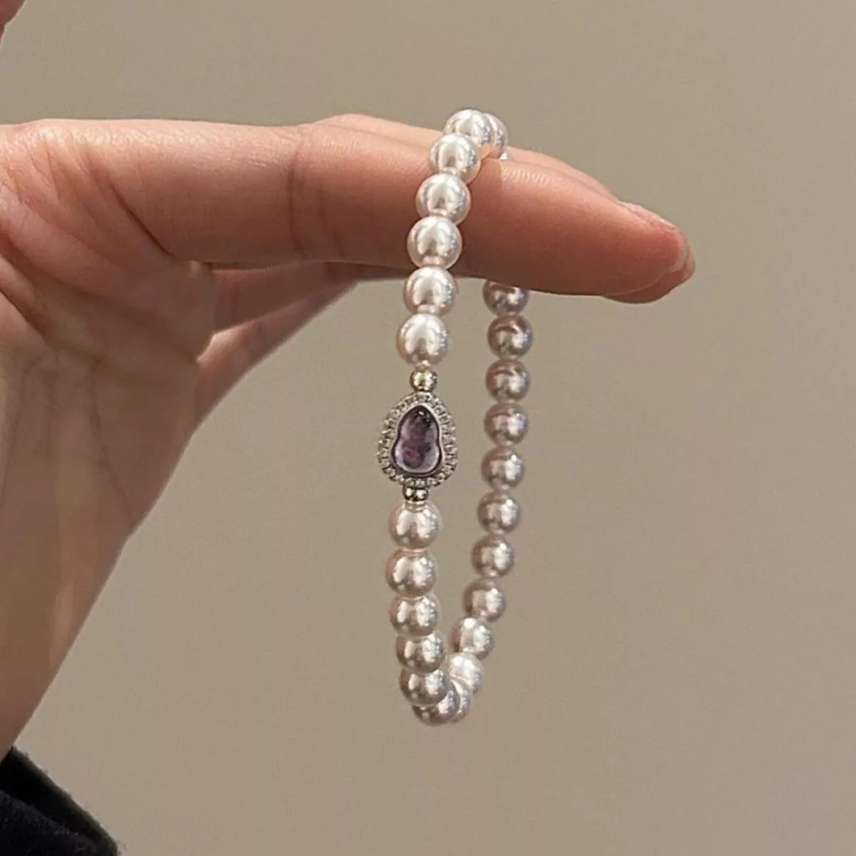 Pearl bracelet with a purple gemstone held by a hand against a neutral background