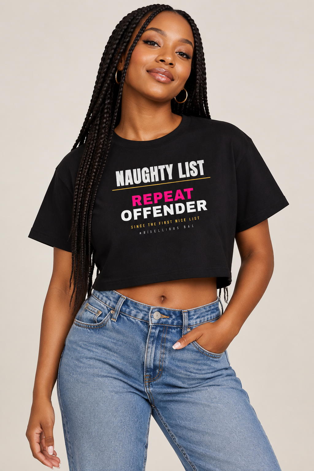 Black cropped graphic t-shirt with naughty list text design, styled with blue jeans on neutral background.
