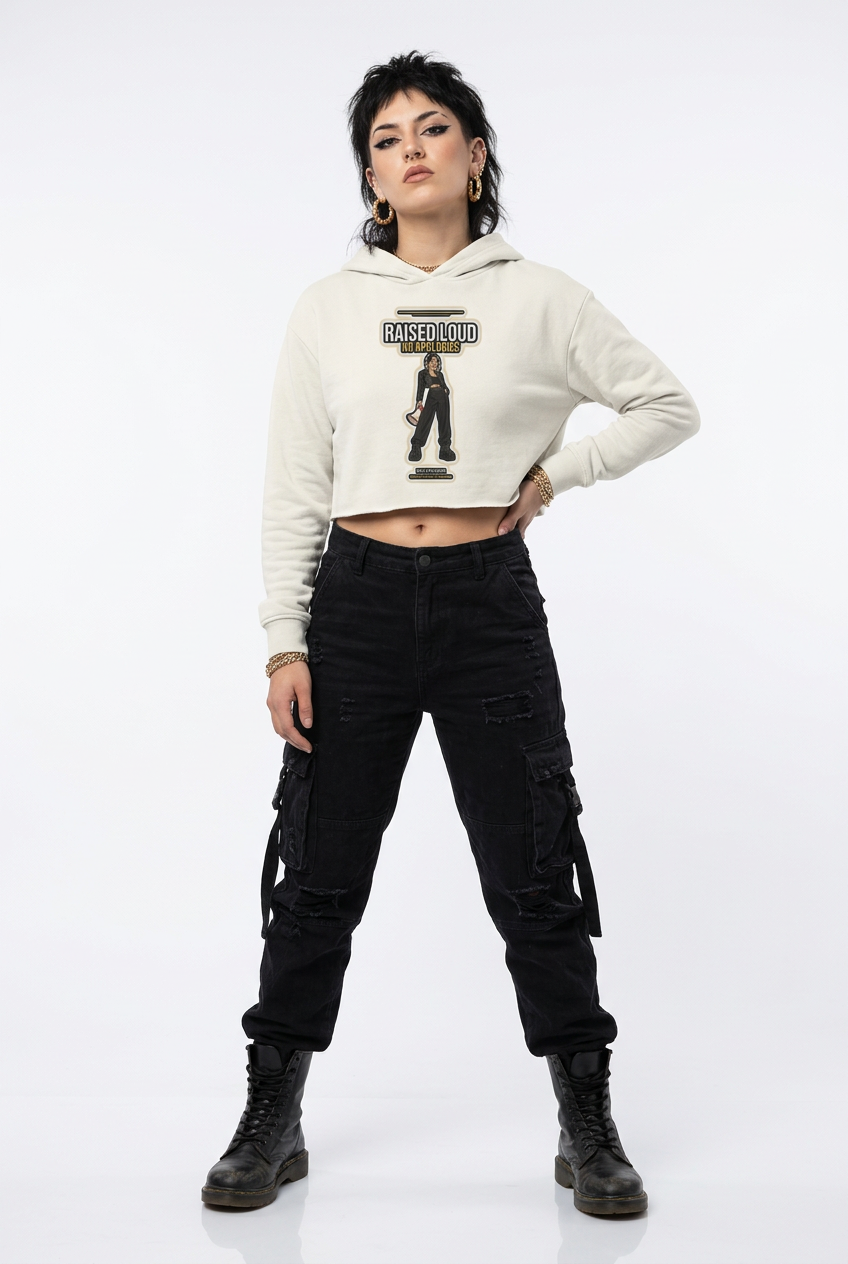 A model stands against a white studio background wearing a cream-colored cropped hoodie with a black graphic print, black cargo pants, and black combat boots.