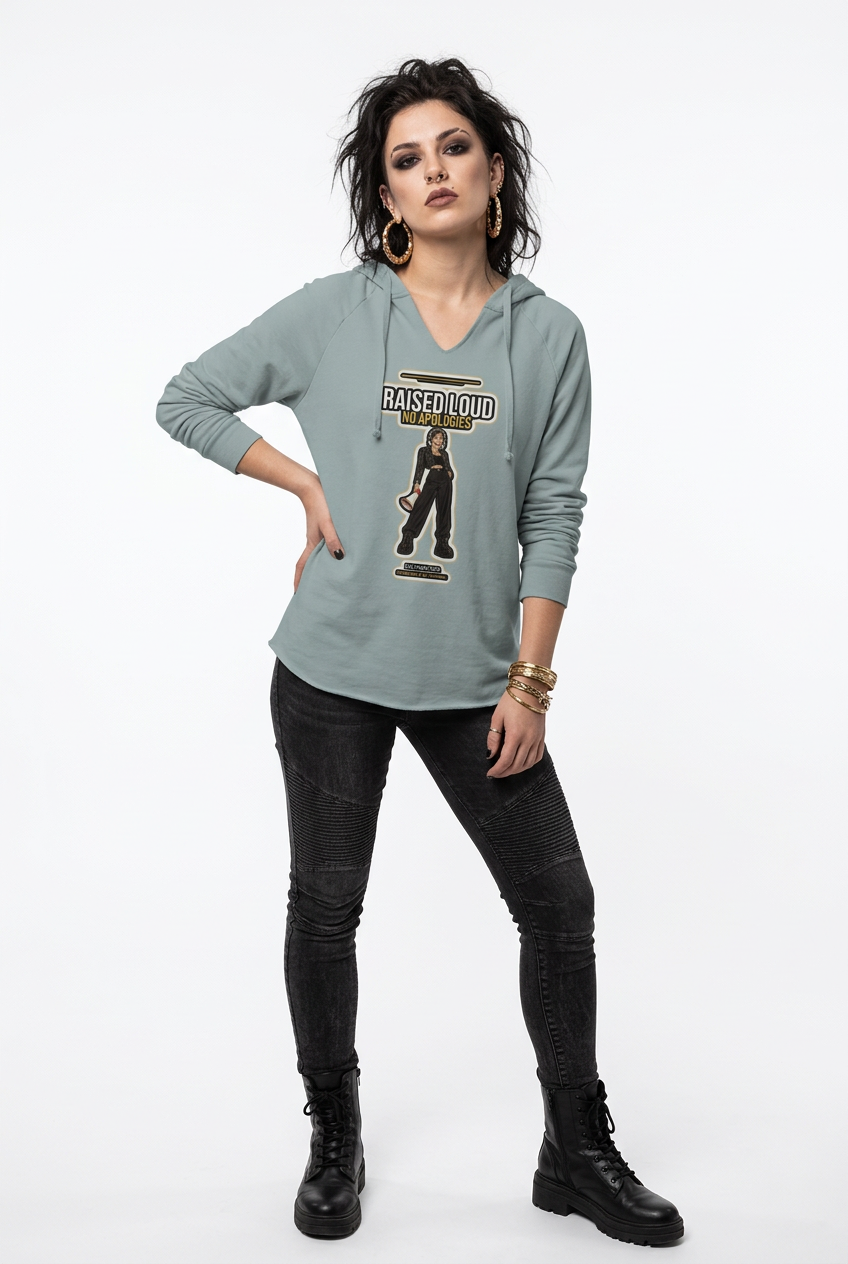 A woman modeling a light sage green long-sleeve hoodie with a graphic print on the front that reads 'RAISED TIDE' and features an illustration of a figure. She is wearing black skinny jeans and black combat boots against a plain white studio background.