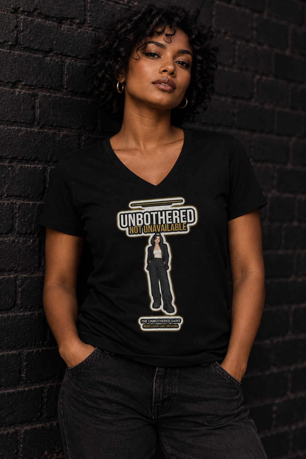 Woman with short curly hair in the black Unbothered Saint v-neck tee against dark brick